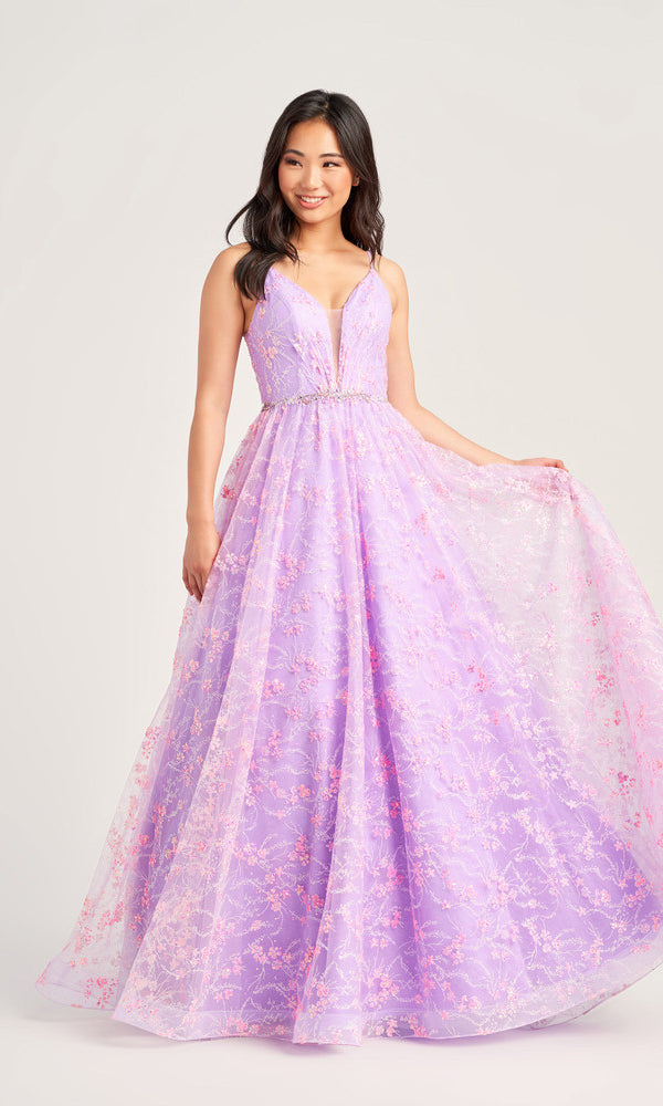 A woman wears the Glitter-Tulle Colette Long Prom Ball Gown CL5288, a floor-length lavender dress with a deep V-neckline, sleeveless design, floral lace overlay, beaded waist, and holds out one side of the shimmering skirt.